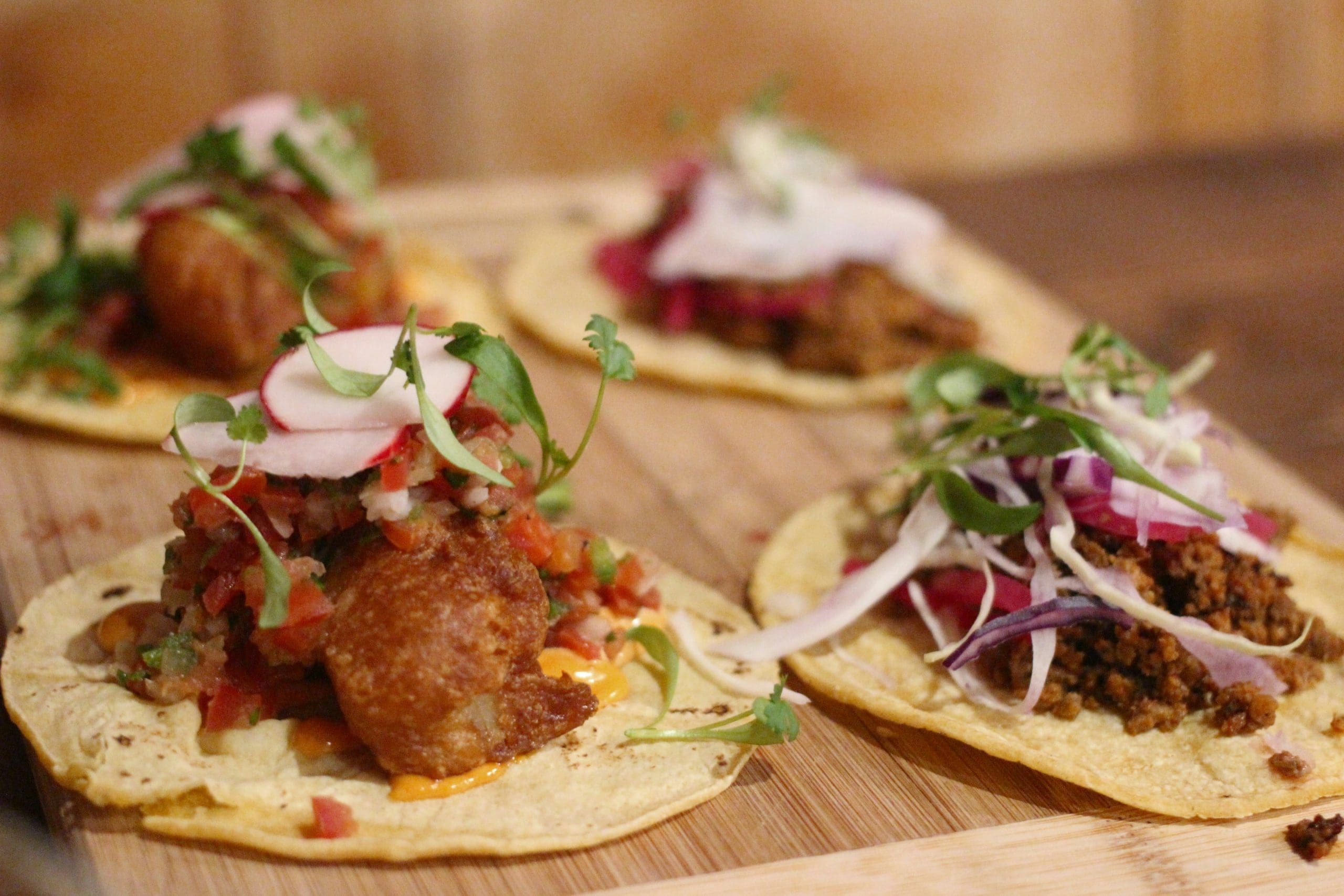 A photo of four tacos on a wooden platter.