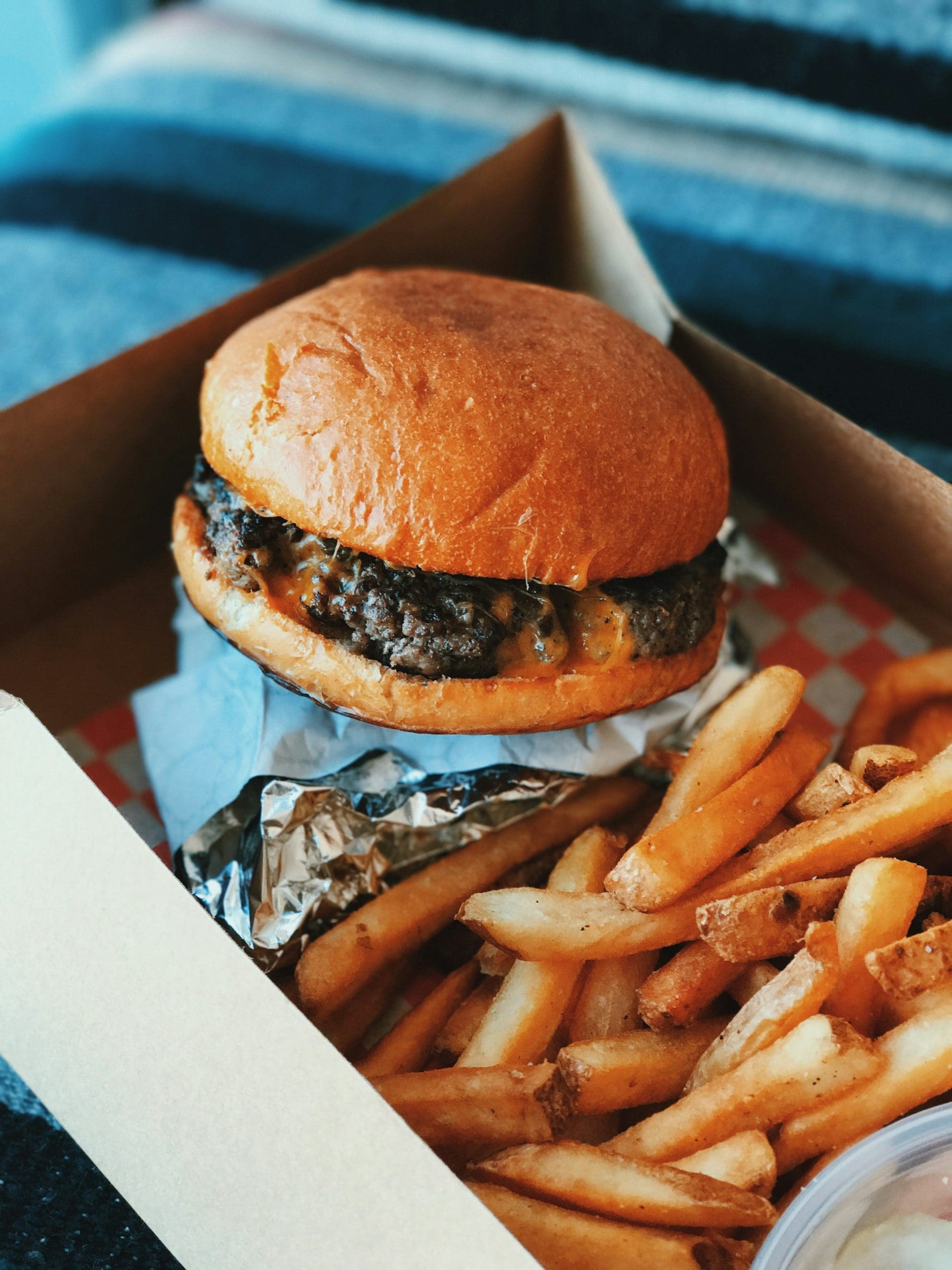 A photo of a cheeseburger with fries inside a cardboard container.